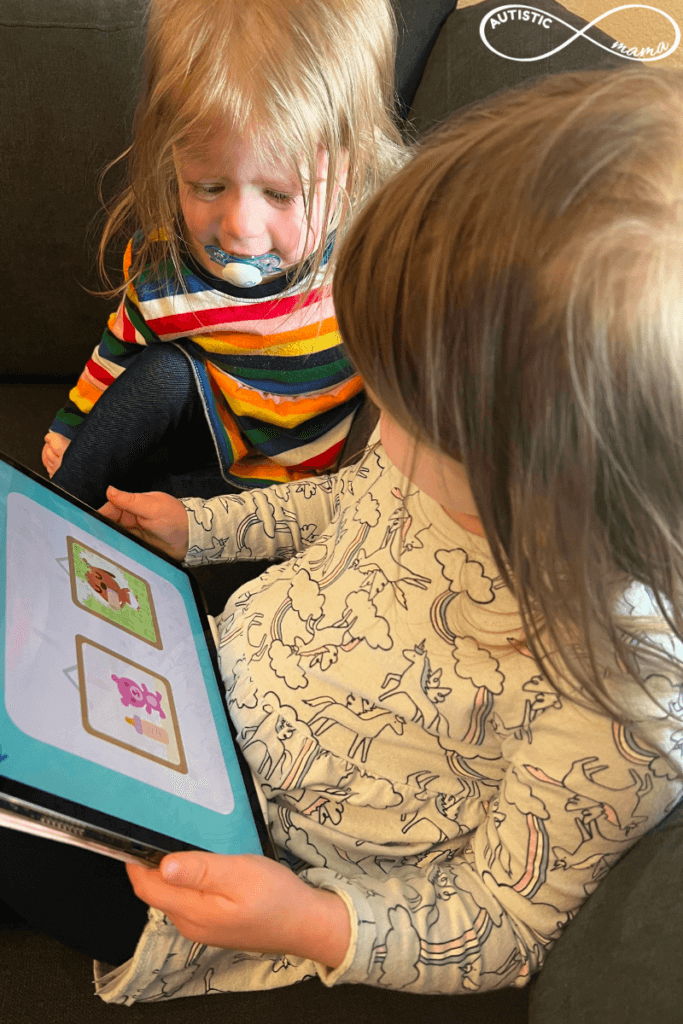 Two children sit next to each other holding a tablet with the screen showing the SAGO Mini First Words App