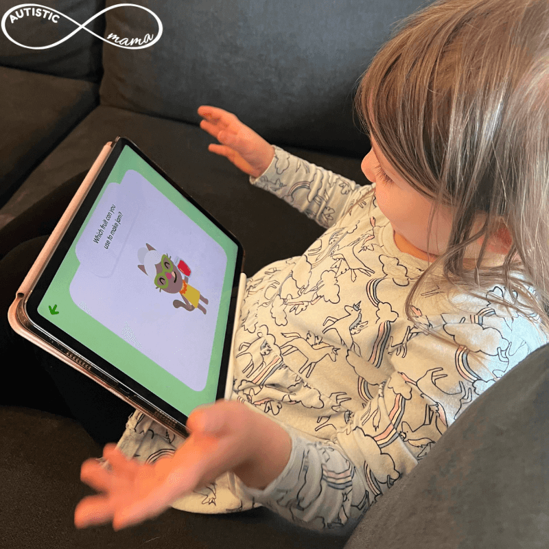 Child sitting down with a tablet screen showing the SAGO Mini First Words App. Child's hands are in the air like they're celebrating.