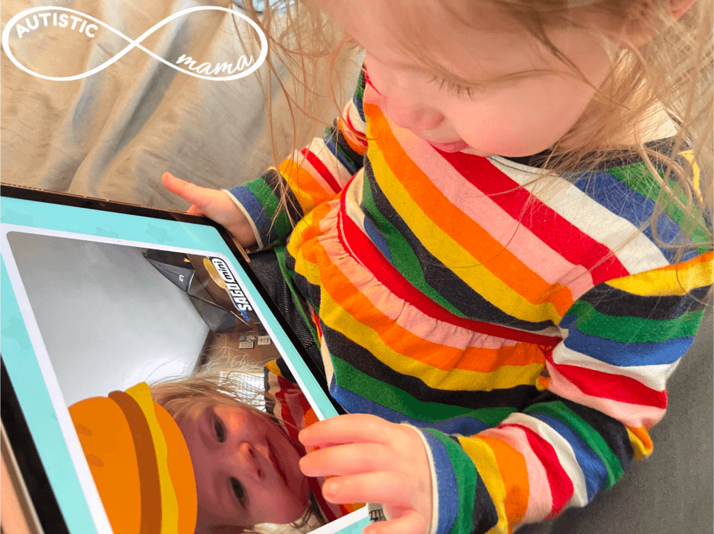 Child sitting down and pointing at a tablet screen showing themselves taking a selfie with the SAGO Mini First Words App